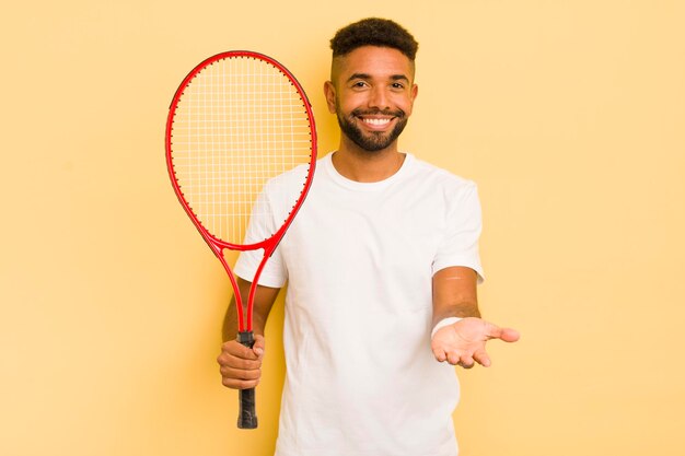 Uomo afro nero che sorride felicemente con amichevole e offrendo e mostrando un concetto di tennis