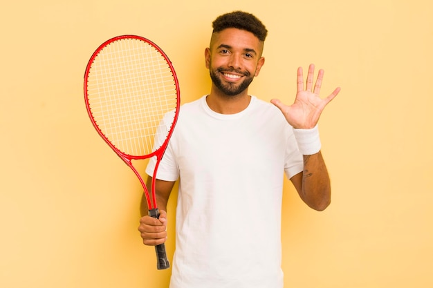 Uomo afro nero sorridente e dall'aspetto amichevole che mostra il concetto di tennis numero cinque