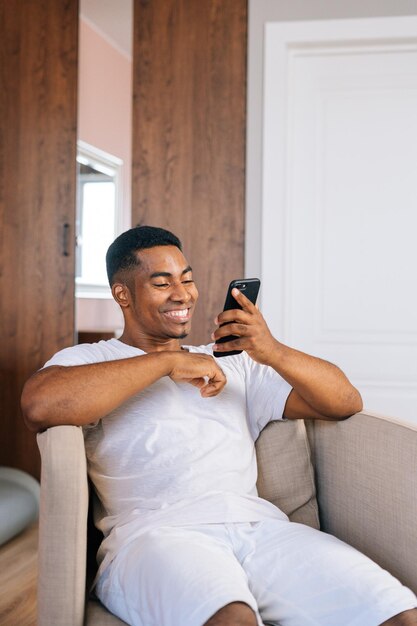 Uomo afroamericano allegro che usa il telefono con la faccia felice e sorridente con il sorriso che mostra i denti