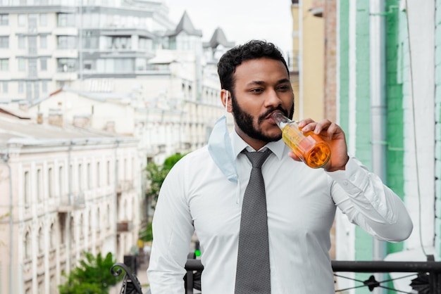 Uomo afroamericano barbuto in maschera medica che beve birra