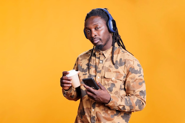 Uomo afroamericano che ascolta musica in studio, naviga su internet utilizzando il telefono cellulare. Allegro adulto che si diverte con le canzoni radiofoniche sulle cuffie, godendosi il suono mp3 durante il tempo libero