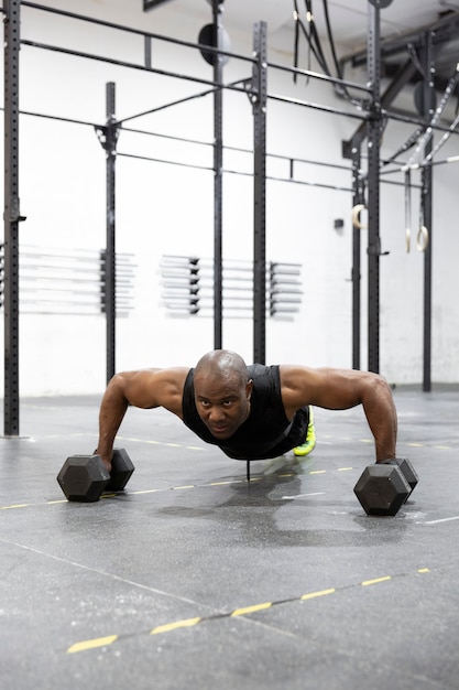 Uomo afroamericano che fa flessioni con kettlebell sul pavimento della palestra. Allenamento intenso della forza del corpo.