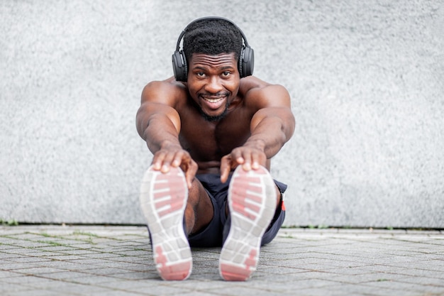 Uomo afroamericano che fa riscaldamento all'aperto contro il muro e ragazzo atletico sorridente che fa sport