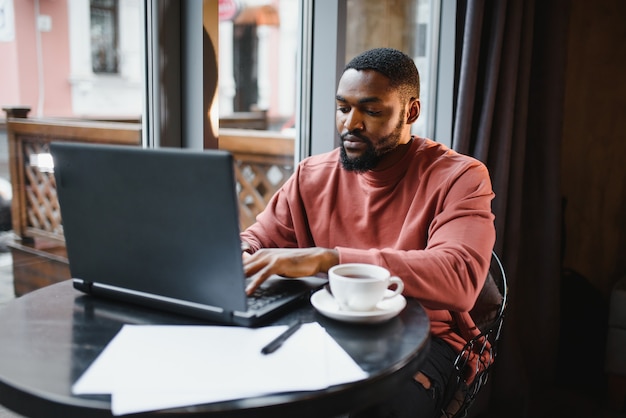 Uomo afroamericano che lavora al computer portatile in un caffè