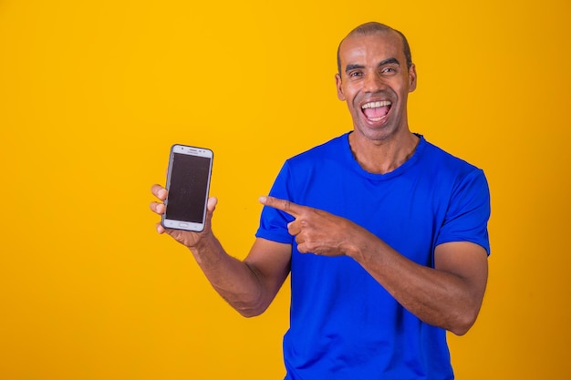 Uomo afroamericano che mostra lo schermo del cellulare che consiglia l'app sorridente alla fotocamera in posa su sfondo giallo dello studio Modello