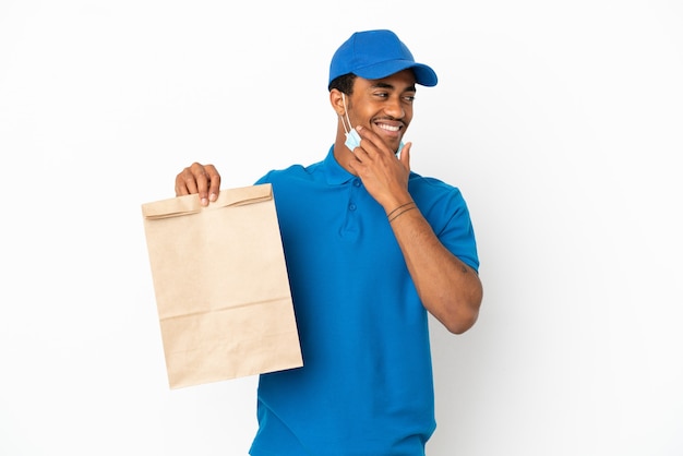 Uomo afroamericano che prende un sacchetto di cibo da asporto isolato su sfondo bianco guardando di lato e sorridente
