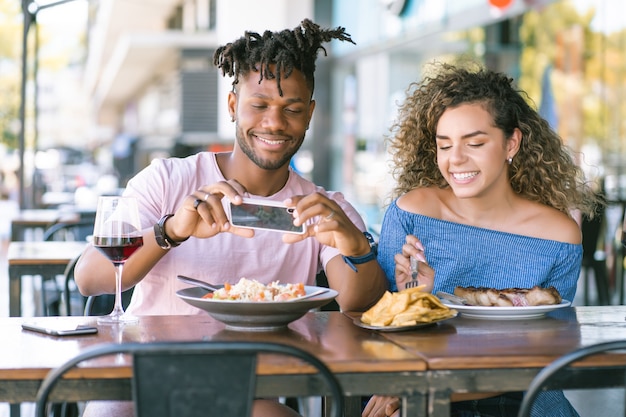 Uomo afroamericano che scatta foto al cibo mentre pranza con la sua ragazza in un ristorante.