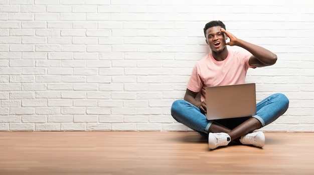 Uomo afroamericano che si siede sul pavimento con il suo computer portatile che intende realizzare la soluzione