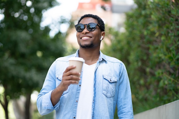 Uomo afroamericano che tiene una tazza di caffè mentre levandosi in piedi all'aperto sulla strada. Concetto urbano.