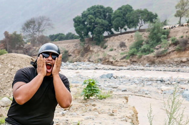 Uomo afroamericano con casco e gesti divertenti vicino a un fiume possente