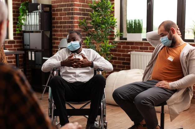 Uomo afroamericano con disabilità che partecipa a un incontro con le persone, ricevendo consulenza contro la dipendenza da alcol durante la pandemia di coronavirus. Pazienti che parlano durante la terapia del gruppo di supporto