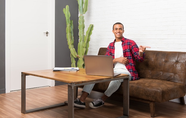 Uomo afroamericano con il computer portatile nel salone che indica dito il lato nella posizione laterale