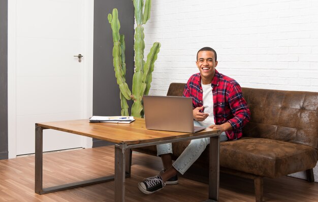 Uomo afroamericano con il computer portatile nel salone che tiene le armi attraversate mentre sorridendo