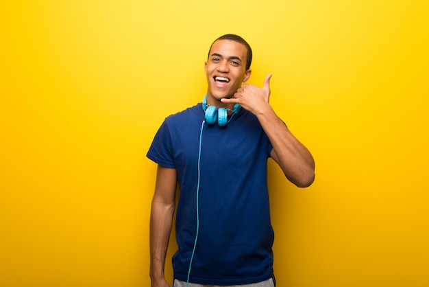 Uomo afroamericano con la maglietta blu su fondo giallo che fa gesto del telefono