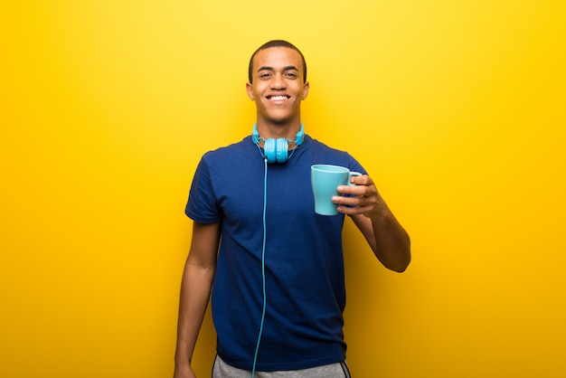 Uomo afroamericano con la maglietta blu su fondo giallo che tiene un caffè caldo