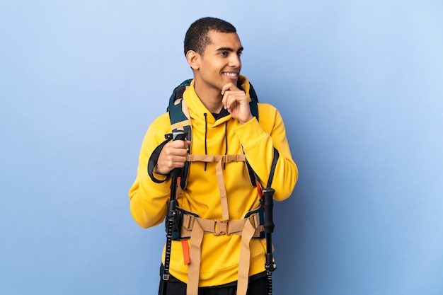 Uomo afroamericano con zaino e bastoncini da trekking che guarda al lato e sorridente