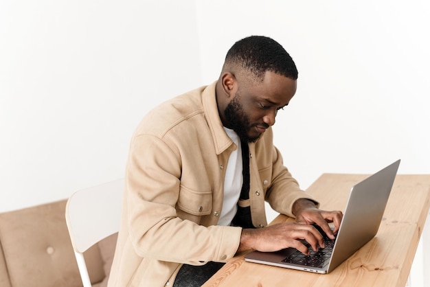 Uomo afroamericano concentrato che lavora sul laptop da casa Il programmatore freelance nero lavora al tavolo