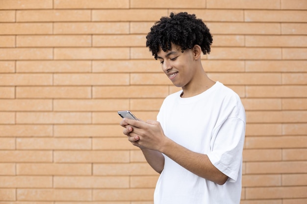 Uomo afroamericano dai capelli ricci sorridente che tiene un telefono e manda un sms agli amici