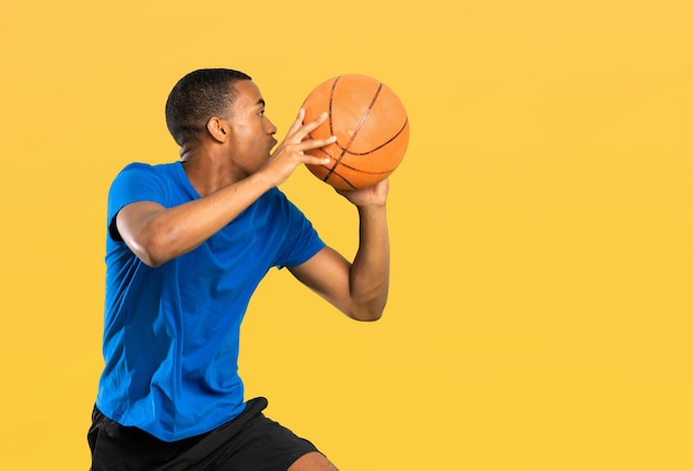 Uomo afroamericano del giocatore di pallacanestro sopra la parete gialla isolata