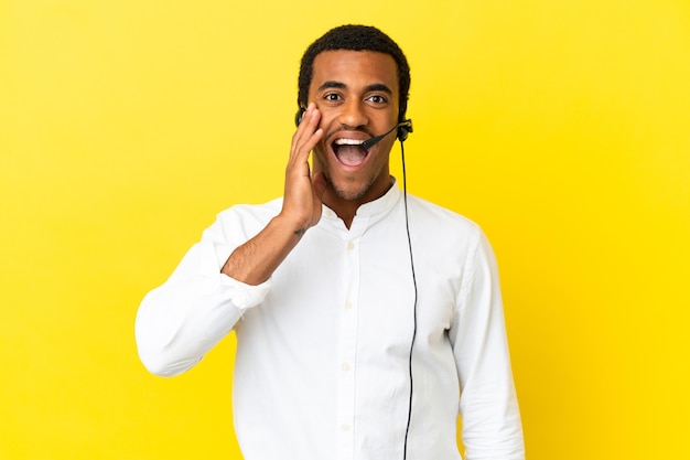 Uomo afroamericano di telemarketing che lavora con un auricolare su sfondo giallo isolato con espressione facciale sorpresa e scioccata