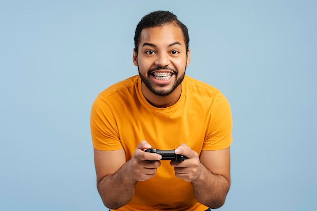 Uomo afroamericano eccitato con un apparecchio ortodontico che tiene in mano un controller di gioco e gioca