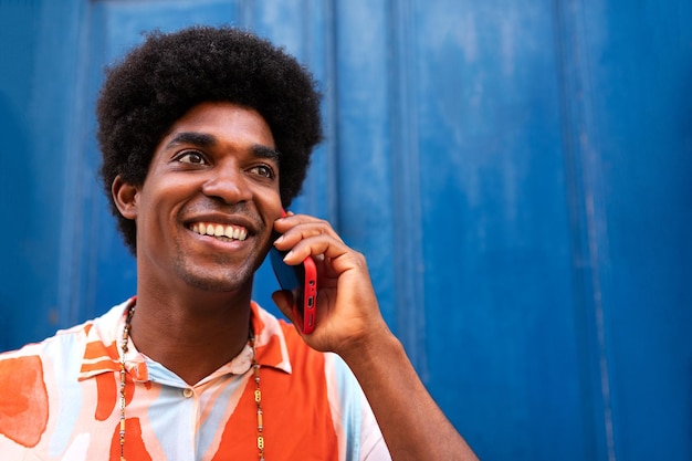 Uomo afroamericano felice sorridente che usa il telefono cellulare per parlare Maschio nero con acconciatura afro su una telefonata in strada Concetto di stile di vita e tecnologia