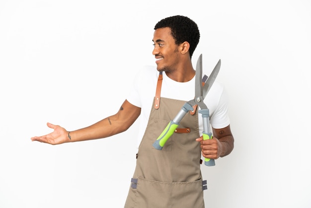 Uomo afroamericano giardiniere che tiene forbici da potatura su sfondo bianco isolato con espressione di sorpresa mentre guarda di lato