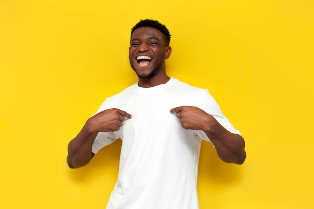 uomo afroamericano gioioso in maglietta bianca mostra le mani a se stesso su uno sfondo giallo isolato