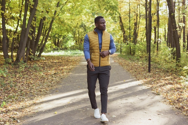 Uomo afroamericano hipster che cammina nel parco autunnale