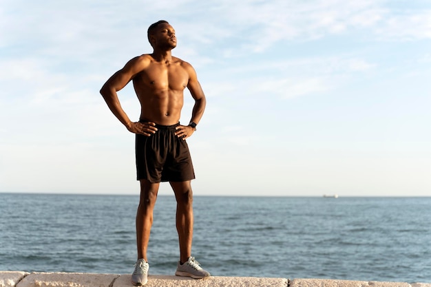 Uomo afroamericano in posa con il torso nudo con mare estivo sullo sfondo