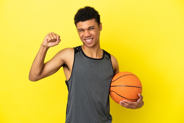Uomo afroamericano isolato su sfondo giallo che gioca a basket e orgoglioso di se stesso