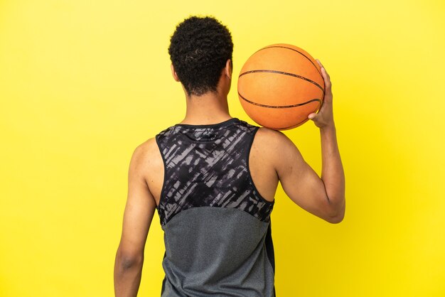 Uomo afroamericano isolato su sfondo giallo che gioca a basket in posizione posteriore