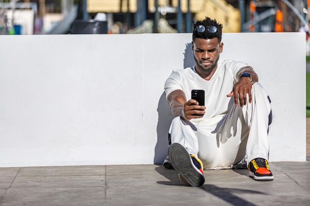 Uomo afroamericano seduto a terra a guardare il cellulare