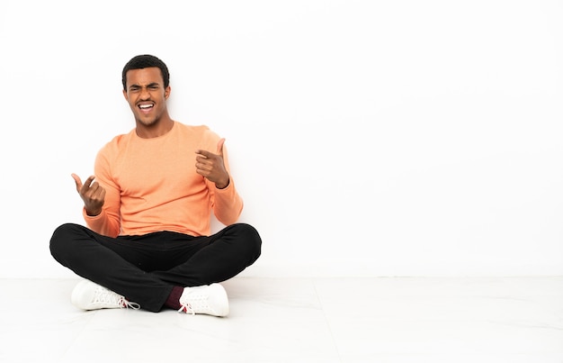 Uomo afroamericano seduto sul pavimento su sfondo copyspace isolato rivolto verso la parte anteriore e sorridente