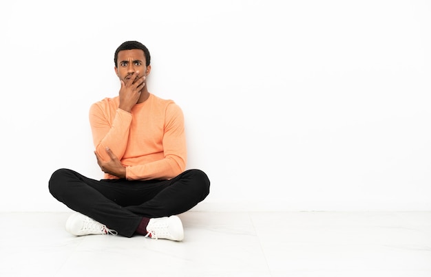 Uomo afroamericano seduto sul pavimento su sfondo copyspace isolato sorpreso e scioccato mentre guarda a destra