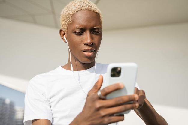 Uomo afroamericano sorridente alla moda che utilizza il telefono cellulare per lo shopping online per strada