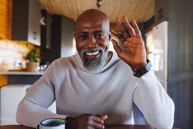 Uomo afroamericano sorridente che fa una videochiamata salutando la telecamera in una baita. Natura, tempo libero, comunicazione e concetto di vacanza.