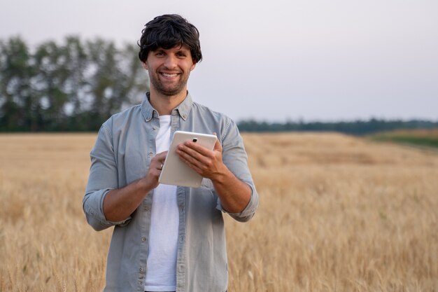 Uomo agricoltore che utilizza computer tablet digitale in piedi in un campo di grano e utilizza app e controlla...