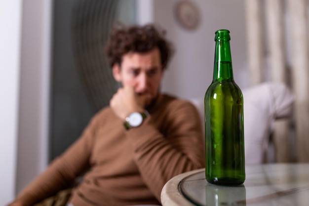 Uomo alcolizzato che cerca una bottiglia di birra, uomo che beve a casa da solo. alcolismo, dipendenza da alcol e concetto di persone - alcolizzato maschio con bottiglia di birra che beve a casa da solo