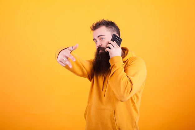 Uomo alla moda che indossa felpa gialla parlando al telefono e mostrando segno ok su sfondo giallo. Smartphone. Uomo alla moda.