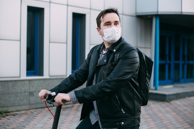Uomo alla moda che per mezzo del motorino elettrico che indossa maschera igienica per prevenire l'infezione