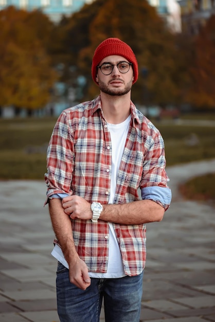 Uomo alla moda con la barba e occhiali da sole in piedi nel parco.