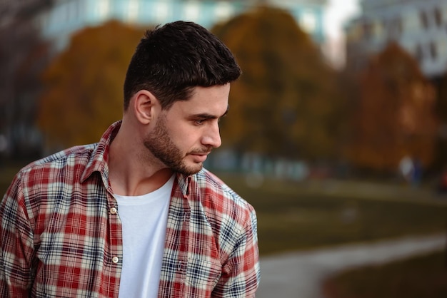 Uomo alla moda con la barba e occhiali da sole in piedi nel parco.