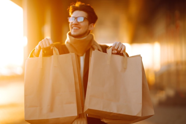 Uomo alla moda con pacchetti di carta dopo lo shopping al tramonto Uomo bello che fa shopping