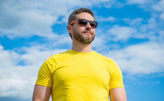 Uomo alla moda in camicia gialla e occhiali da sole all'aperto su sfondo cielo