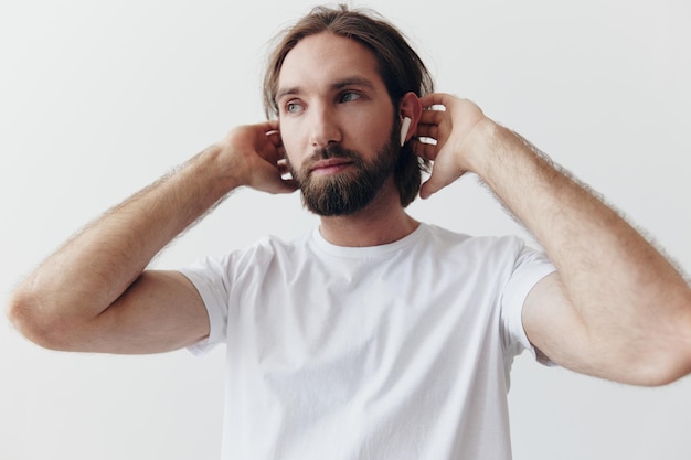 Uomo alla moda in una maglietta bianca con cuffie wireless nelle orecchie divertendosi ad ascoltare la musica sorridere su uno stile di vita di sfondo bianco