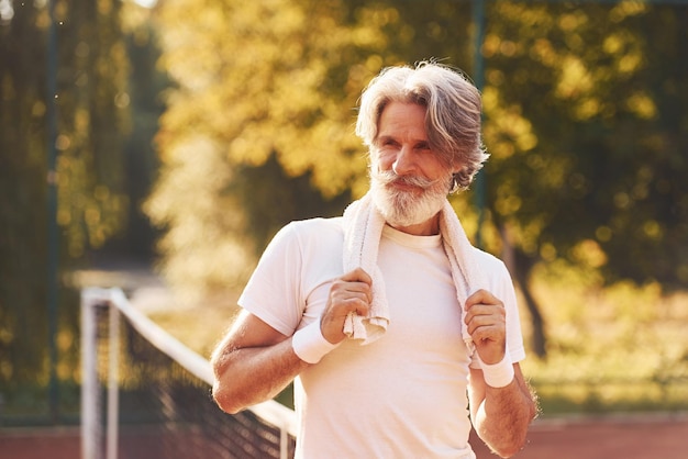 Uomo alla moda senior in camicia bianca e pantaloncini sportivi neri sul campo da tennis