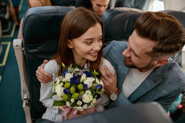 Uomo allegro che abbraccia donna con fiori in aereo