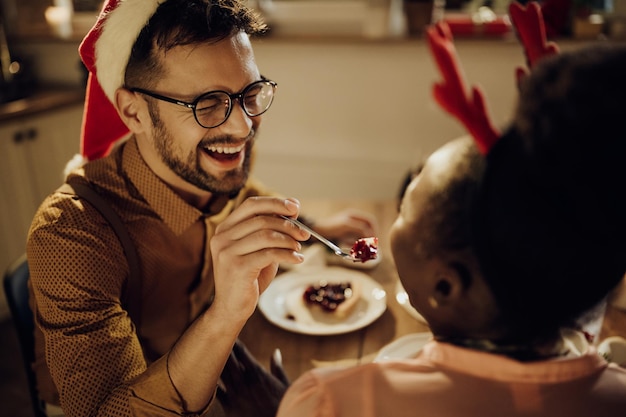 Uomo allegro che alimenta la sua ragazza durante la cena di Natale a casa