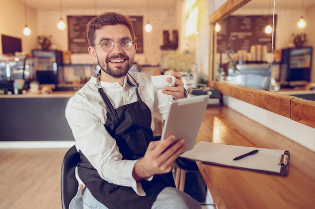 Uomo allegro che beve caffè e utilizza il computer tablet nella caffetteria